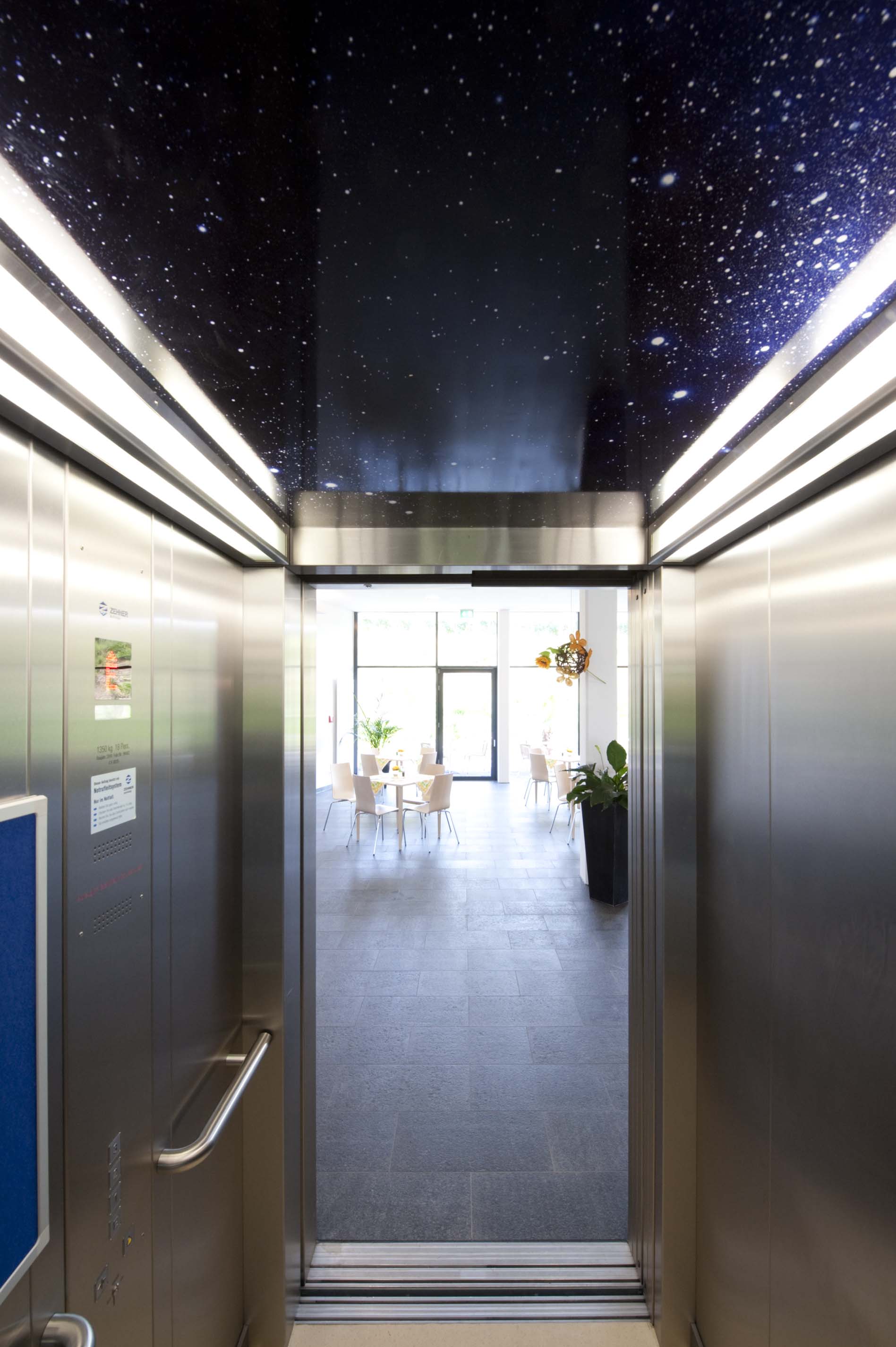 Innenansicht eines Aufzugs mit Nachthimmel an der Decke und offenen Türen