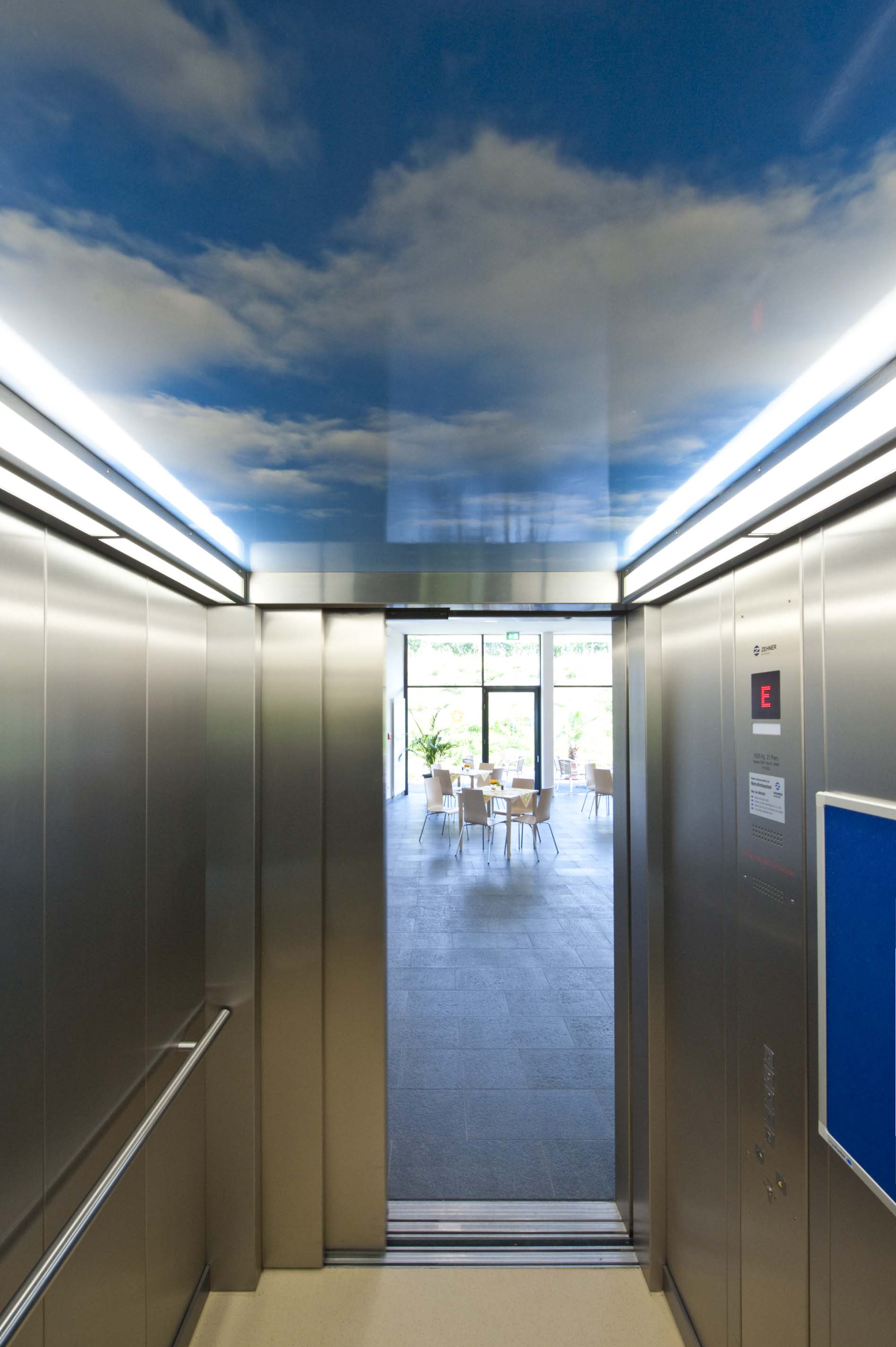 Innenansicht eines Aufzugs mit Tageshimmel an der Decke und offenen Türen